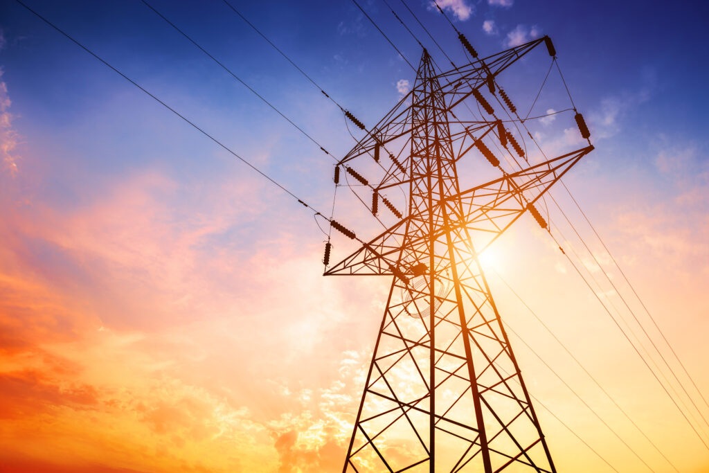 Fotografia de uma torre de alta tensão metálica, vista de baixo, com cabos elétricos a estenderem-se para o céu.